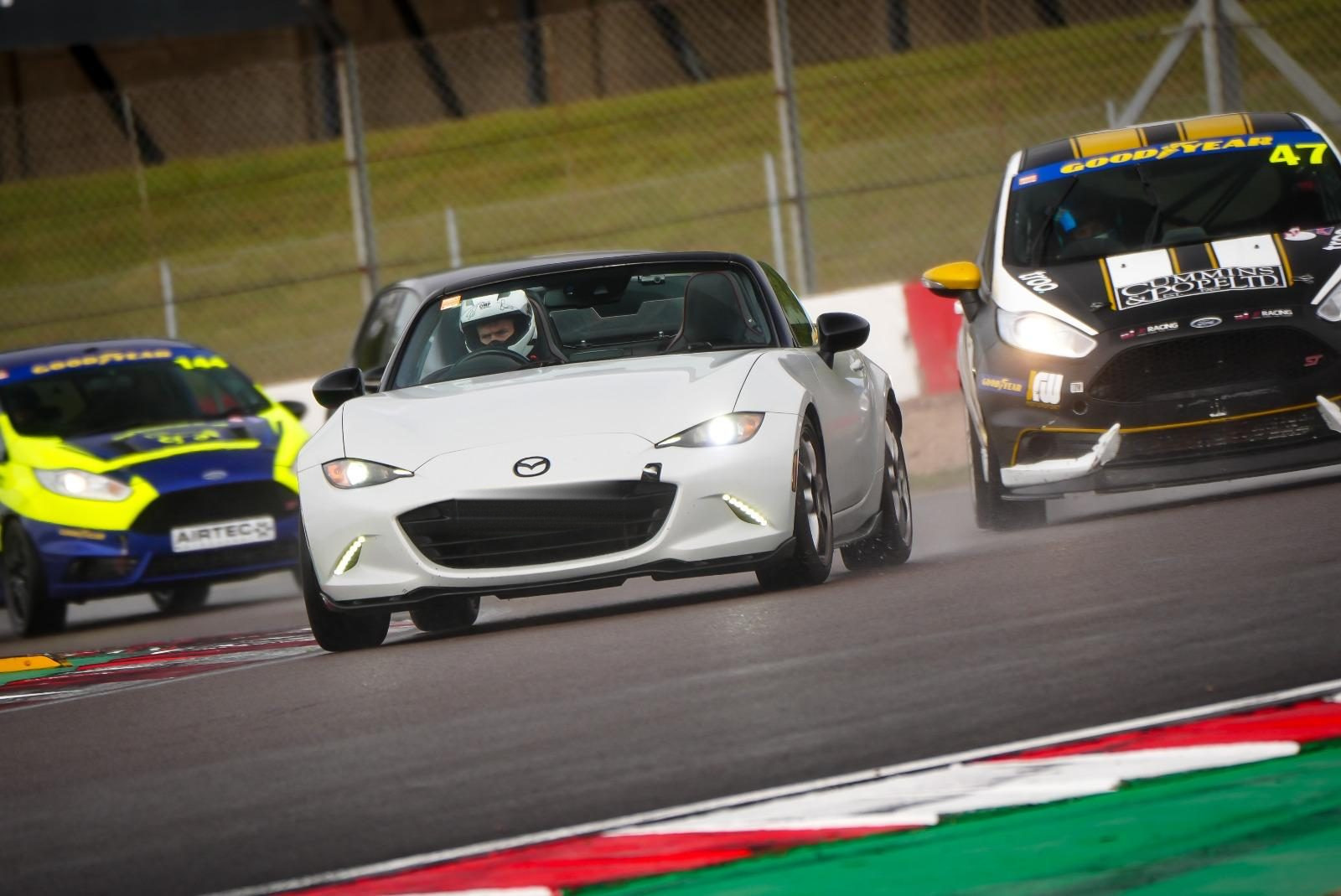 A white Mazda MX-5 on track, leading two race-prepared hatchbacks